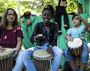 Ein Erwachsener mit Gitarre, drei Kinder, singend und trommelnd, lachen in die Kamera. Im Hintergrund ein Affe als Handpuppe.