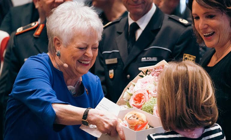 Die Stadträtin Malischewski überreicht einen Blumenstrauß und eine Geschenkschachtel.