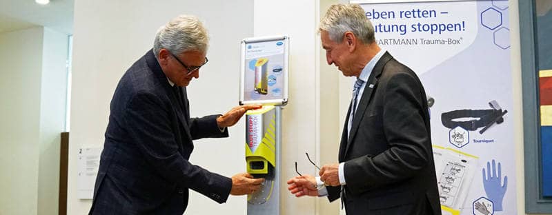 Oberbürgermeister Gunter Czisch und Prof. Dr. Thomas Wirth von der Traumastiftung ziehen einen Beutel mit Hilfsmitteln aus einem Spender.