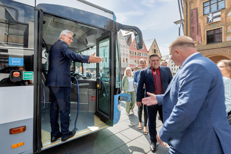 Oberbürgermeister Czisch hält die Hand aus der Bustür einladend ausgestreckt.