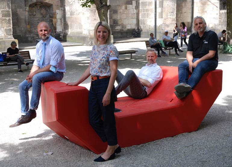 Drei Männer und eine Frau sitzen auf einem roten Sitzelement auf dem Münsterplatz