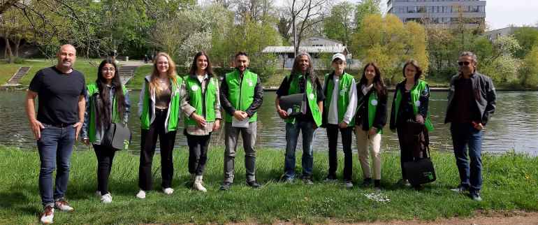 Eine Gruppe von Frauen und Männern an der Donau. Einige tragen grüne Westen, die sie Als Ulmer Müllscouts ausweisen.