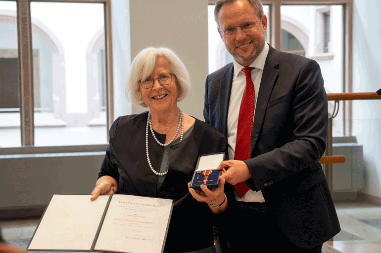 Oberbürgermeister Martin Ansbacher hält das Bundesverdienstkreuz in die Kamera. Die Preisträgerin Dorothee Kühne die offizielle Urkunde des Bundespräsidenten