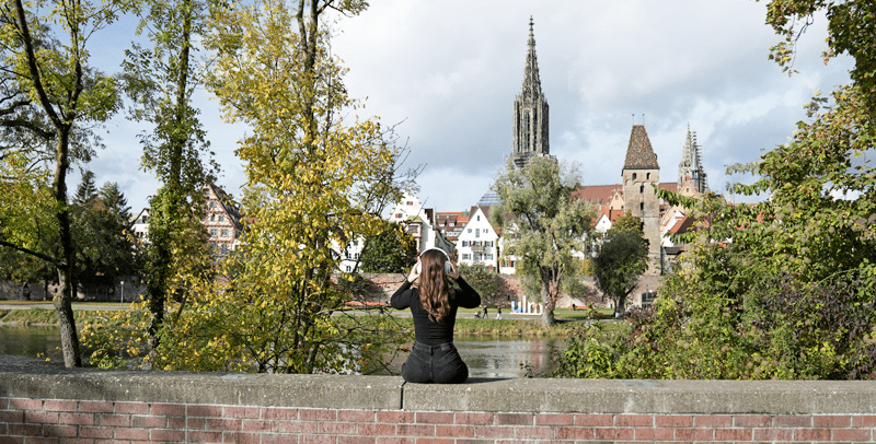 Eine junge Frau mit Kopfhörern sitzt auf der Stadtmauer.