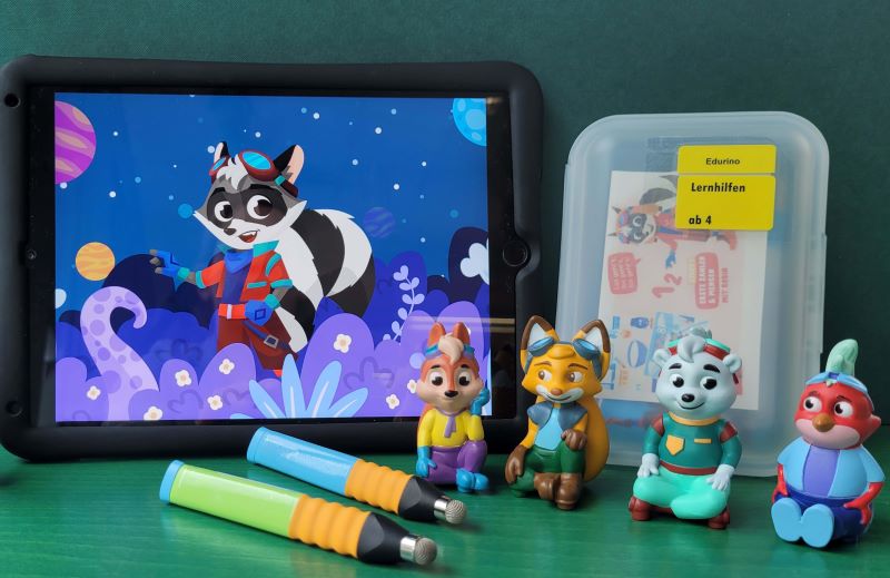 Ein Tablet mit einer Abbildung einer Comicfigur. Daneben vier Edurino-Figuren und zwei Edurino-Stifte