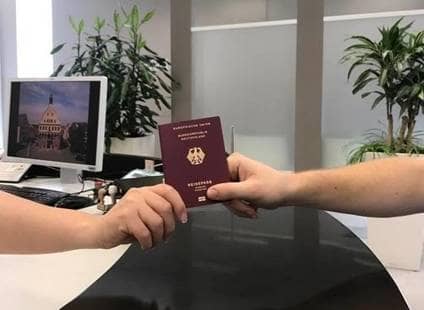 Eine Mitarbeiterin überreicht einem Bürger einen Reisepass.