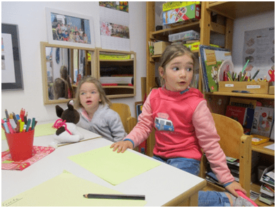 Zwei Mädchen im Kindergarten sitzen an einem Tisch mit Blättern und Stiften