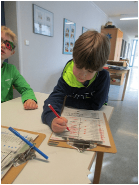 Ein Kind, welches mit rotem Filzstift etwas in eine Liste malt bzw. schreibt.