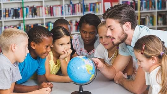 Kinder sitzen mit Lehrkraft um einen Globus