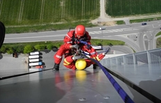 Ein Höhenretter der Feuerwehr Ulm seilt sich mit einem Verletztendarsteller in hundert Metern Höhe an der gläsernen Außenfassade eines Siloturmes an zwei Seilen ab. 