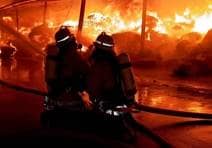 Angriffstrupp der Feuerwehr Ulm mit Schutzkleidung und Atemschutzgerät löscht mit einem C-Rohr aus 10 Meter Abstand eine im Vollbrand stehende Lagerhalle bei Nacht.