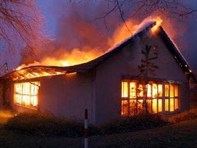 Ein eingeschossiges Schulgebäude brennt in voller Ausdehnung in der Morgendämmerung. Flammen schlagen aus dem eingestürzten Dach. Über zwei Fensterfronten sieht man die Flammen im Inneren des Gebäudes.