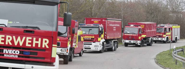 Verschiedene Gefahrgutfahrzeuge der Ulmer Feuerwehr aufgereiht an einer Straße an einer Einsatzstelle; in der Mitte das Dreiachs-Wechselladerfahrzeug mit dem Abrollbehehälter zur Dekontamination von Verletzten.