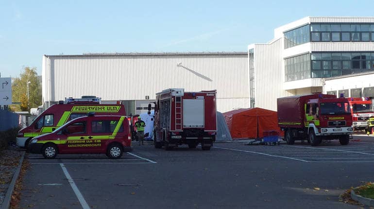Fahrzeuge des katastrophenschutzes vor dem aufgebauten Personendekontaminationsplatz aus Zelten bei einer Katastrophenschutzübung mit vielen kontaminierten Verletzten.