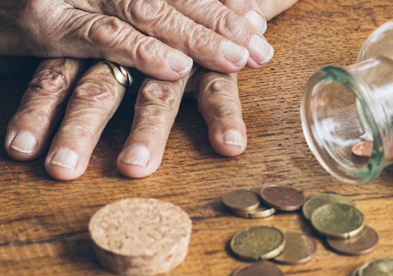 Eine ältere Dame hat die Hände übereinandergelegt, vor ihr auf dem Tisch liegen ein paar Geldmünzen.