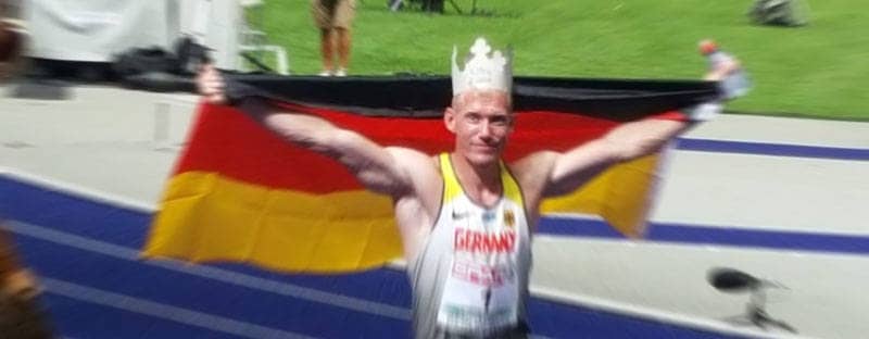 Arthur Abele läuft in Sportkleidung und mit einer Deutschlandfahne im Stadion.