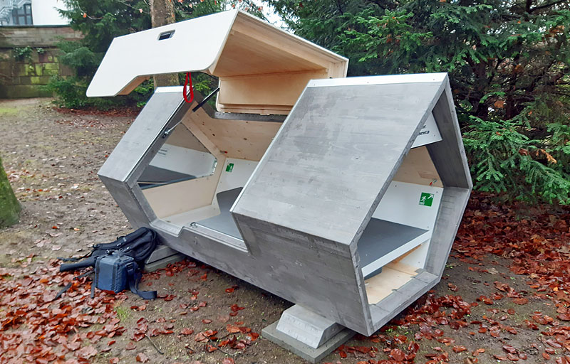 Menschengroße Box aus Holz und Blech mit einer Liegefläche, die man von innen abschließen kann.