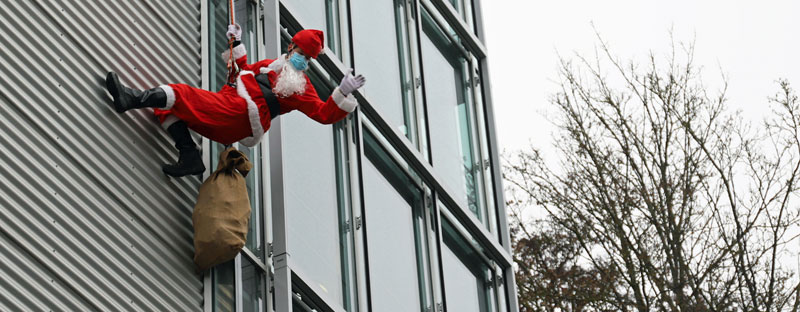 Ein Mann in einem Nikolauskostüm lässt sich an einer gläsernen Hausfassade mit einem Seil hinab