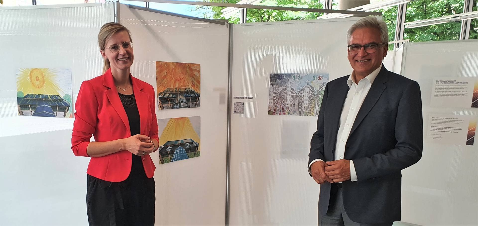 Katrin Albsteiger und Gunter Czisch vor einer Stellwand mit gemalten Bildern