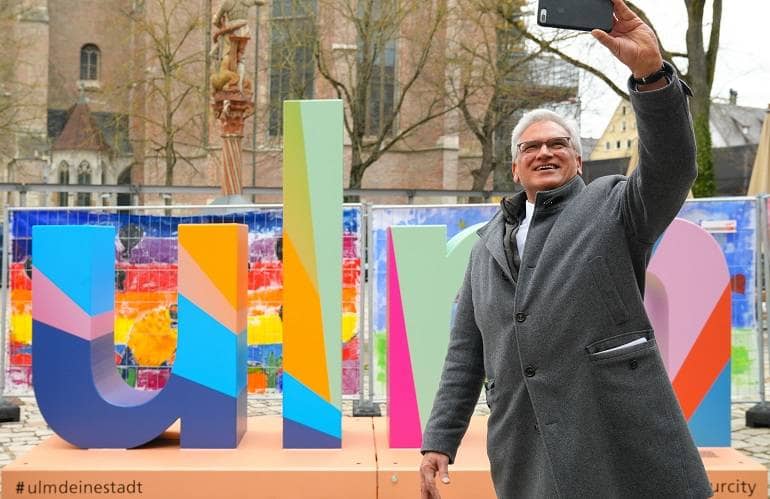 Oberbürgermeister Gunter Czisch macht ein Selfie vor dem Selfie-Point der Stadt Ulm. Im Hintergrund ist das Münster zu sehen.