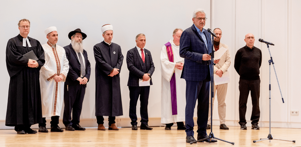 Oberbürgermeister Czisch mit weiteren acht Personen, die religiöse Trachten tragen, auf der Bühne im Haus der Begegnung.