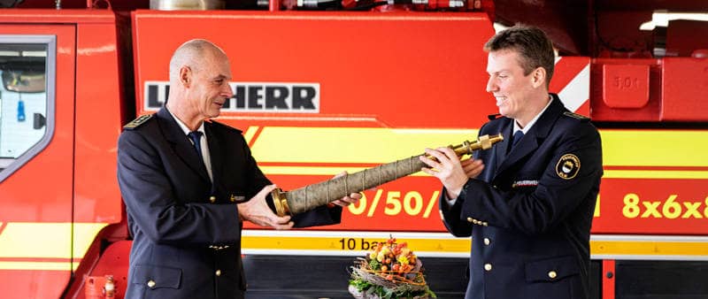 Der scheidende und der neue Feuerwehrkommandant vor einem Feuerwehrwagen