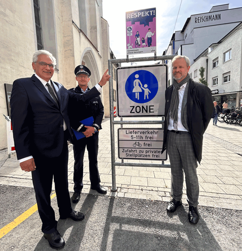 Gunter Czisch, Tim von Winning und ein uniformierter Polizist vor einem Verkehrsschild