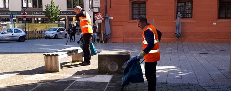 Zwei Mitarbeiter der Entsorgungsbetriebe sammeln Müll von der Straße