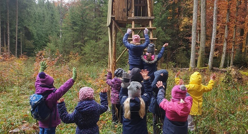 Eine Gruppe von Kindern erkundet im Wald einen Hochsitz.