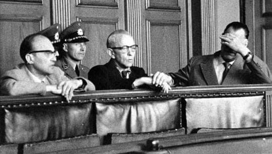 Drei Männer sitzen auf einer Anklagebank in einem Gerichtssaal