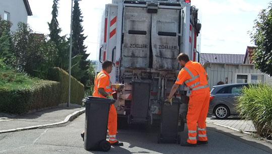 Zwei Mitarbeiter der Müllabfuhr beladen einen Abfuhrwagen.
