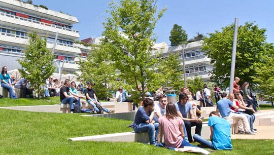 Studierende sitzen vor einem Universitätsgebäude
