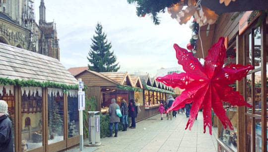 Ein aus Papier gefalteter Stern hängt über einem Stand auf dem Weihnachtsmarkt.