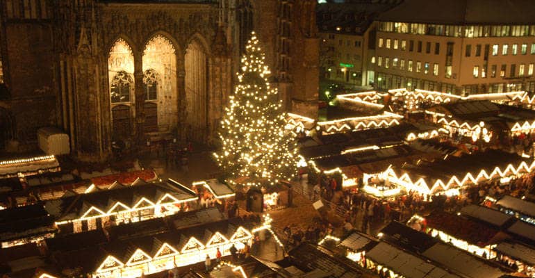 Ein mächtiger Weihnachtsbaum auf dem Münsterplatz leuchtet im Dunkeln, drum herum sind Buden aufgebaut.