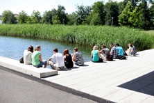 Studierende sitzen im Außenbereich der Hochschule an dem kleinen, quadratsich angelegten Teich.