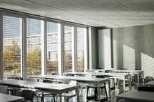 Seminarraum mit Tischen und Stühlen und raumhohen Fenstern.