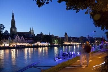 Ufer der Donau bei Nacht mit der Ulmer Stadtfront im Hintergrund.