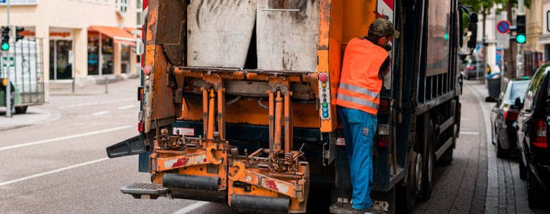 Ein Mitarbeiter eines Abfuhrunternehmens steht hinten auf einem Müllwagen.