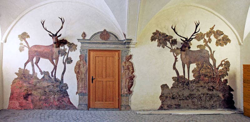 Unter den Bögen eines Gewölbes sind zwei Hirschfiguren an der Wand kunstvoll aufgemalt.