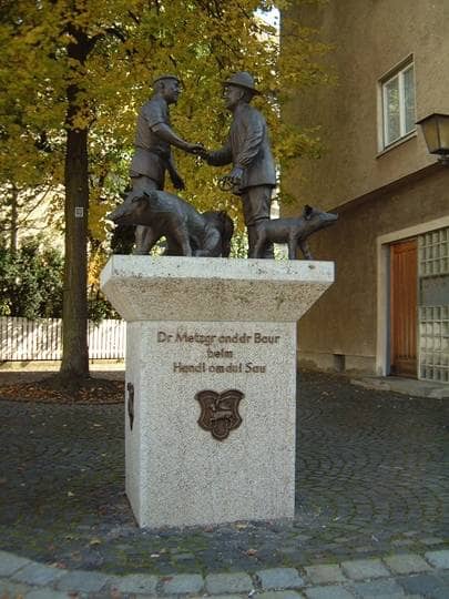 Eine Bronzeplastik zeigt drei Schweine sowie zwei Männer, die per Handschlag ein Geschäft besiegeln.
