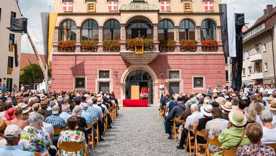 Hunderte Menschen sitzen im Sommer auf dem Weinhof und blicken zum Balkon des Schwörhauses, auf dem der Oberbürgermeister spricht.