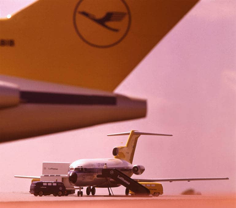 Zwei kleine Flugzeugmodelle. Auf einer ist das Logo der Lufthansa zu erkennen: Ein mit wenigen Strichen gezeichneten Kranich, der nach oben aufsteigt und von einem Kreis umgeben ist.