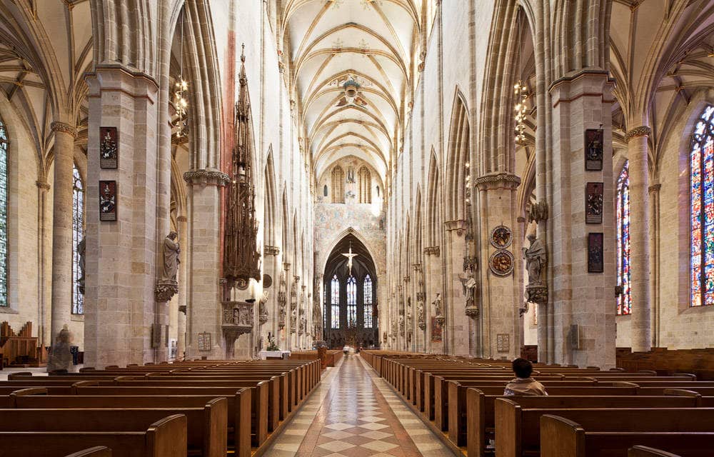 Kirchenbänke im Ulmer Münster, eingerahmt von hohen Säulen und einer großen, gewölbten Decke