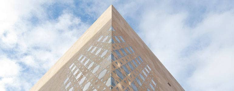Eine Ecke eines quaderförmigen Gebäudes ragt in den Himmel. In die Fassade sind sechseckige Davidsterne aus Glas eingelassen, in denen sich der Himmel spiegelt.