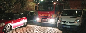 Ein Feuerwehrauto fährt in der Nacht durch eine eng beparkte Straße.