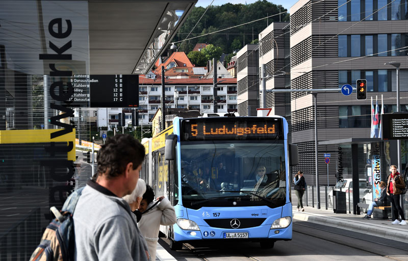 Ein Bus hält an einer Haltestelle, an der Fahrgäste warten.